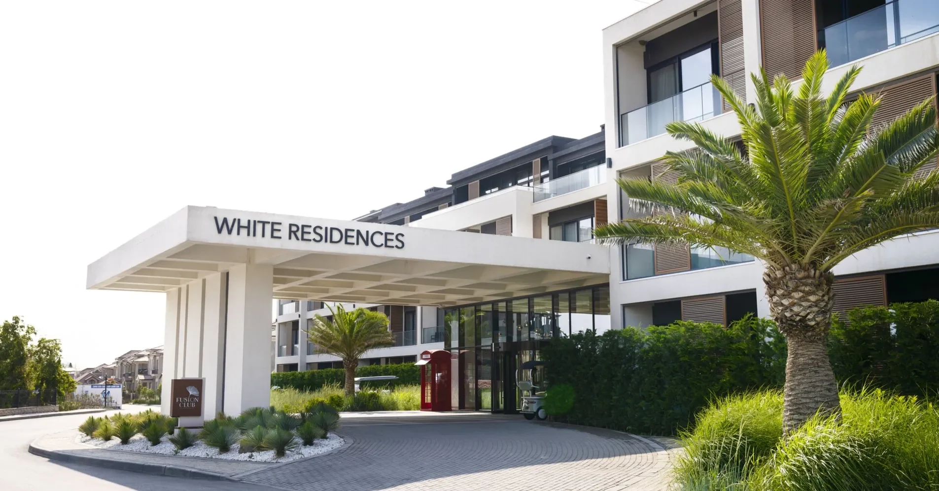 כניסה מתחת לסוכך עם הכיתוב WHITE RESIDENCES, ומאחוריה בניין עם תריסי עץ